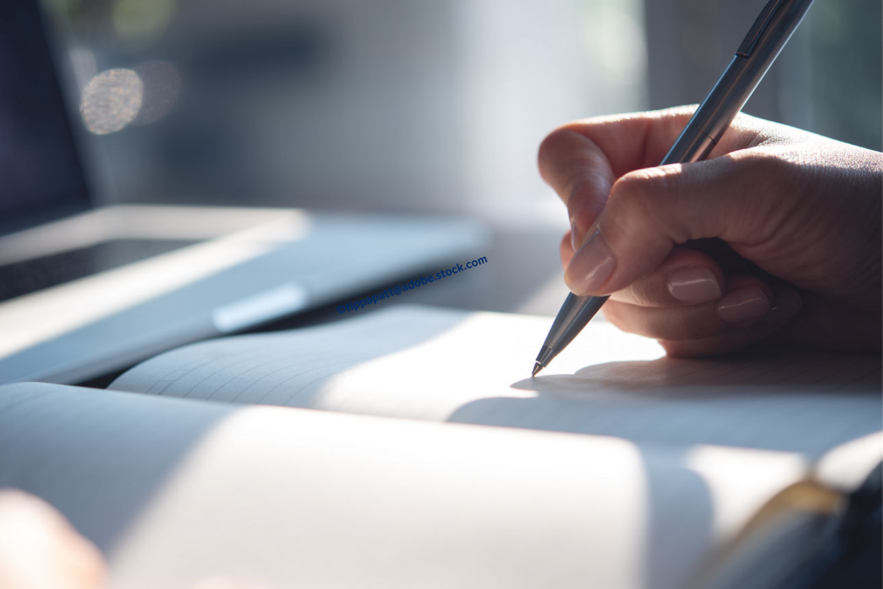 Jemand schreibt mit einem Stift in ein Notizbuch