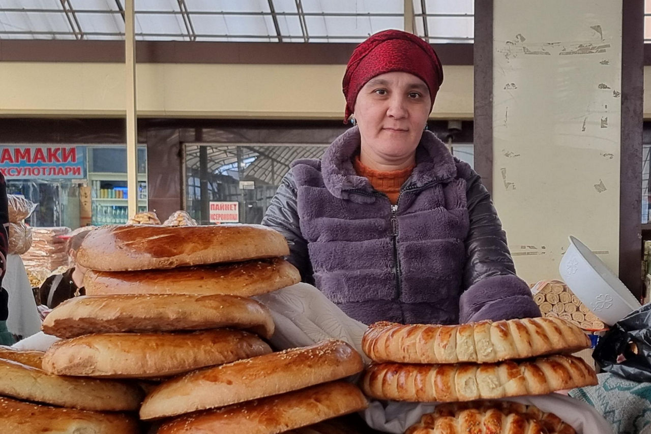 Frau steht an ihrem Stand, vor ihr ein Stapel Brote