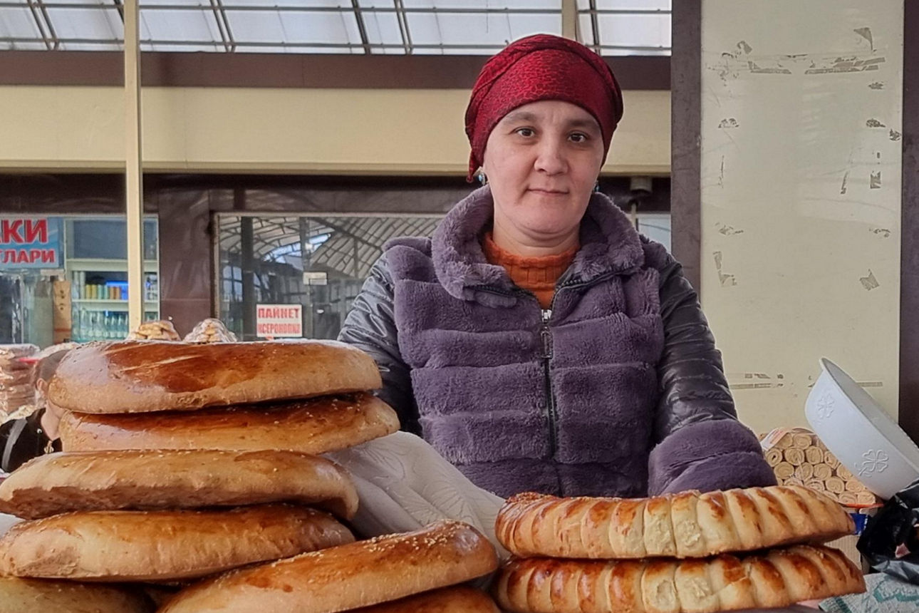 Marktverkäuferin mit frisch gebackenem Brot in verschiedenen Formen vor Gebäude mit kyrillischer Schrift