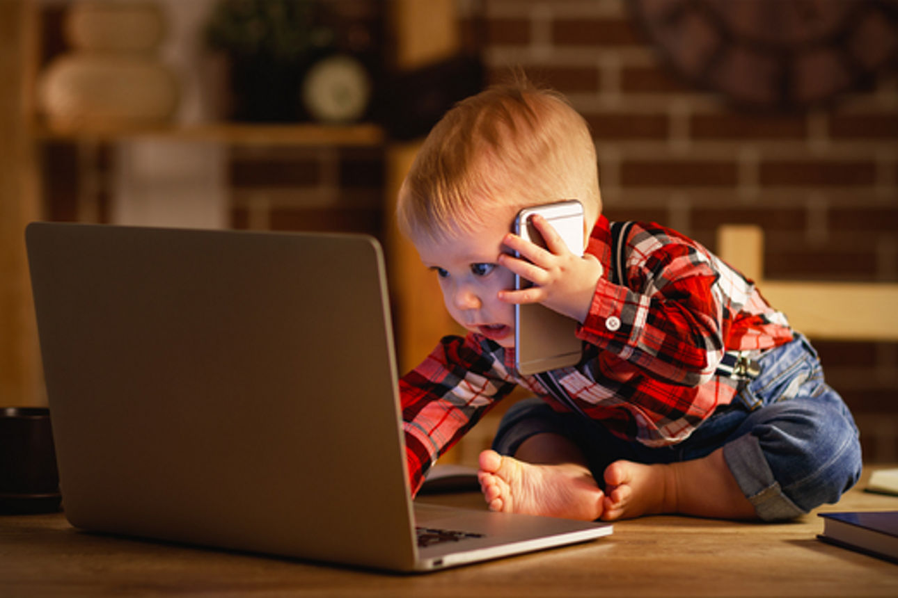 Ein Kind sitzt mit Handy am Ohr am Laptop