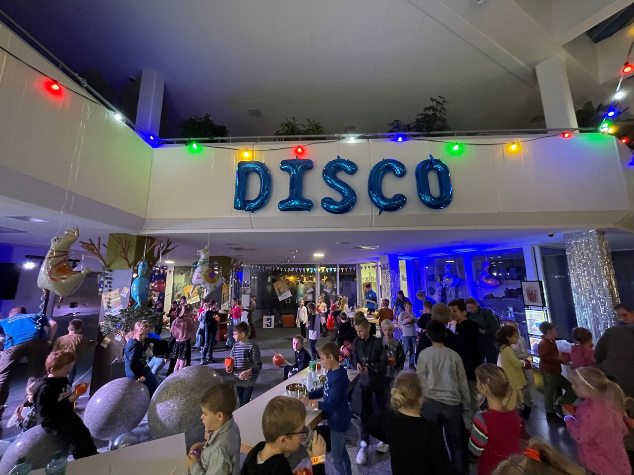 Eine große Gruppe von Kindern ist in einem hell erleuchteten Raum zu einer Disco-Party versammelt.