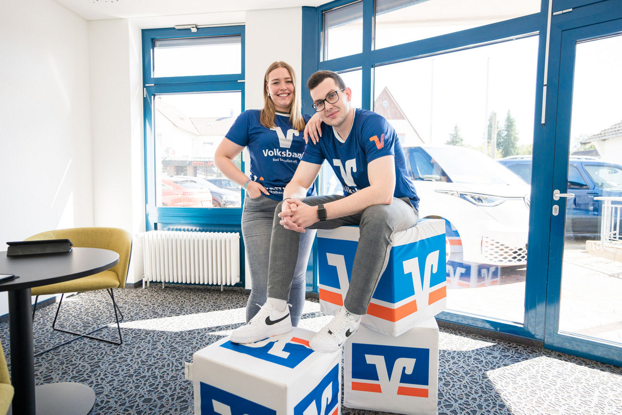 Zwei junge Kollegen der VBBS, die auf bzw. an Volksbank-Würfeln stehen