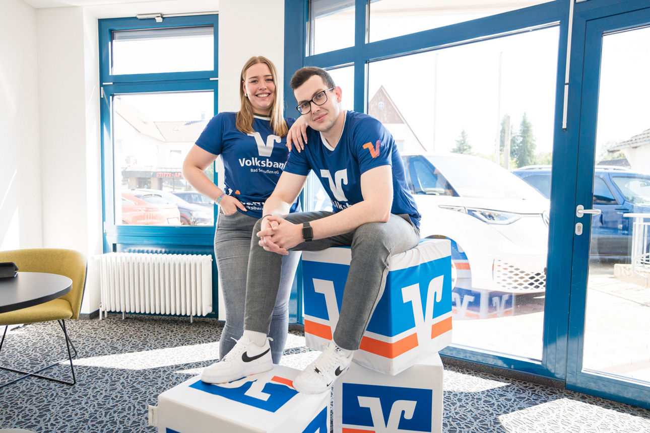 Zwei junge Kollegen der VBBS, die auf bzw. an Volksbank-Würfeln stehen
