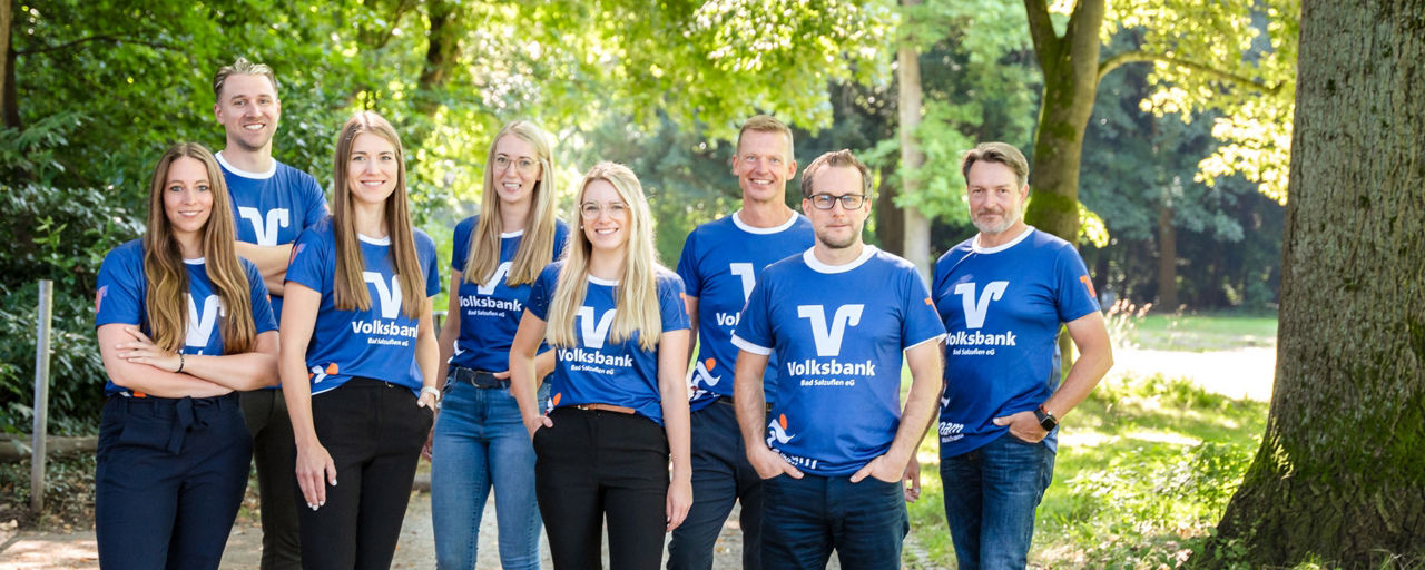 Mitarbeiter der Volksbank Bad Salzuflen tragen Volksbank-Trikots und stehen gemeinsam zwischen Bäumen