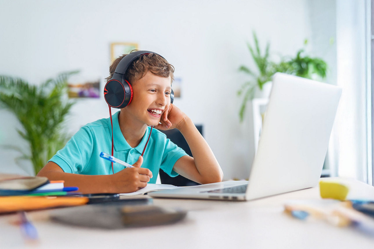Ein Schüler mit einem Headset sitzt lächelnd vor einem Laptop