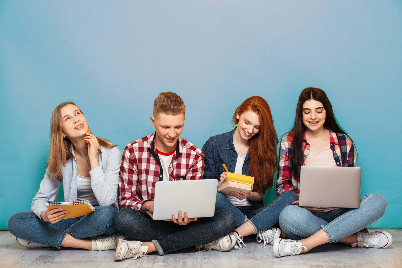 Vier junge Menschen sitzen mit Laptops und Büchern auf dem Boden