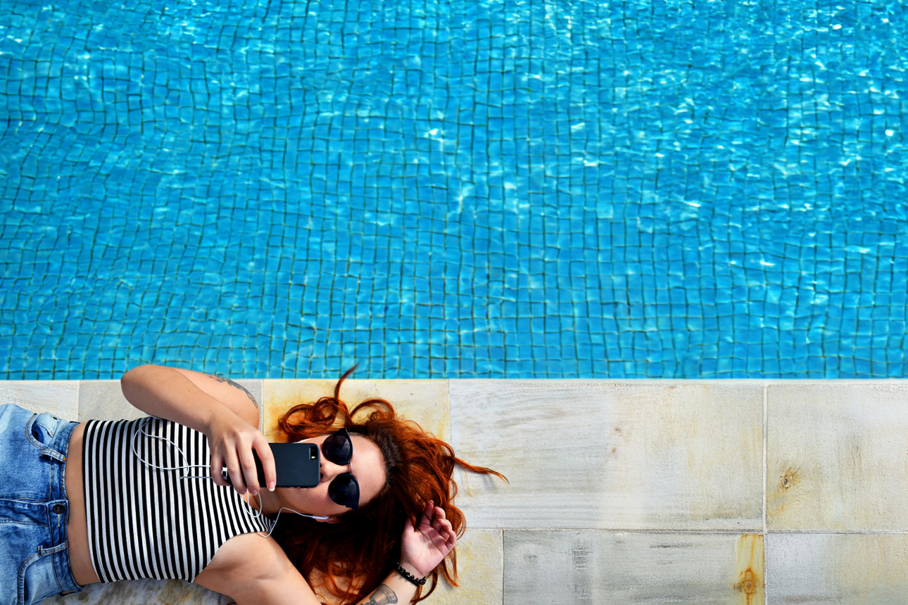 Junge Frau mit Smartphone liegt am Poolrand