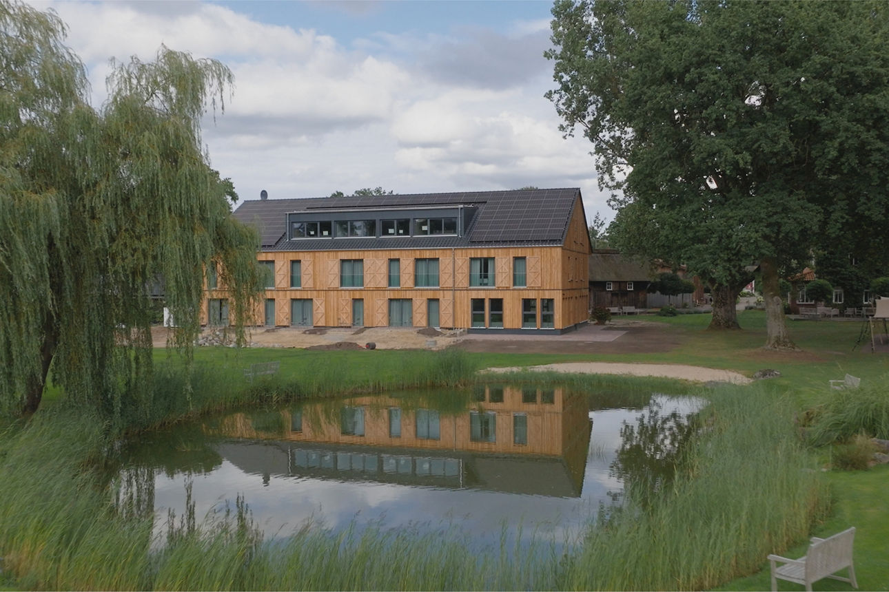 Hotelneubau im Hintergrund, davor ein großer Teich, Bäume und viel Grün