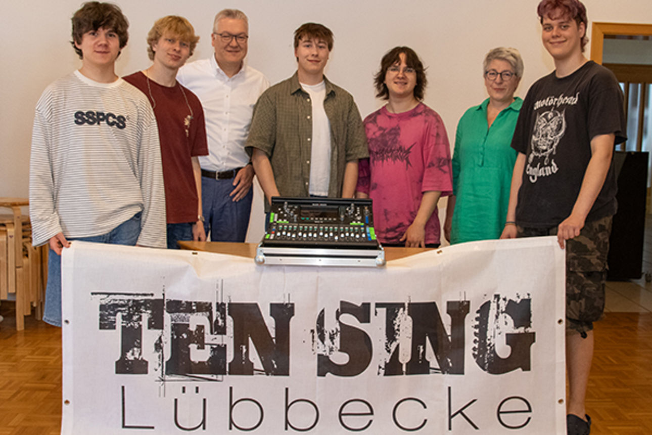 Gruppenfoto hinter einem großen Banner und mit einem Mischpult