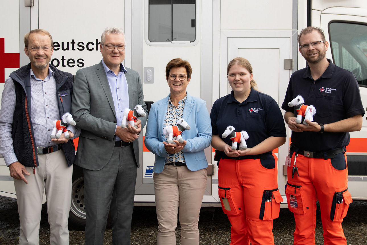 Fünfergruppe mit Stofftieren in den Händen vor einem Rettungswagen