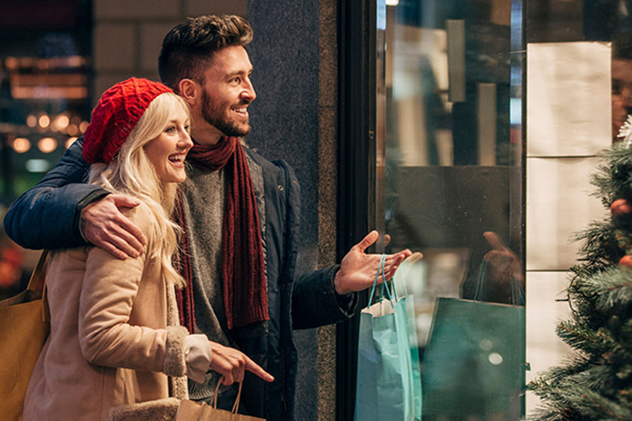 Junger Mann und junge Frau sind beim weihnachtlichen Einkaufsbummel und tragen ihre Einkäufe.