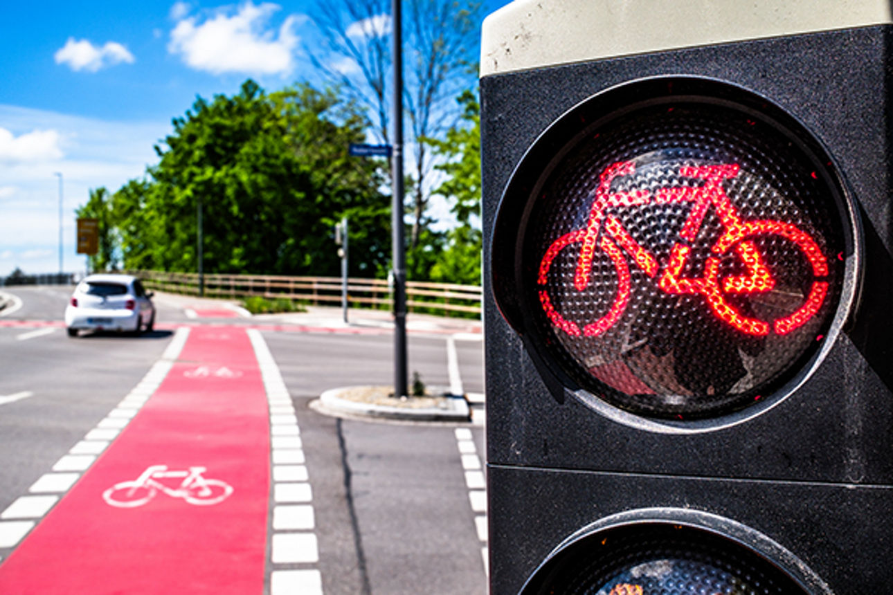 Zweigeteiltes Foto: links eine rote Fahrradspur auf einer Straße, rechts eine Rot zeigende Radlerampel