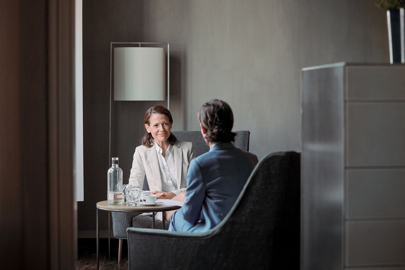 Eine lächelnde, reife Unternehmerin blickt eine Kollegin an. Geschäftsfrauen besprechen in einer Besprechung ihre Strategie. Sie führen in einem Hotel ein Gespräch.
