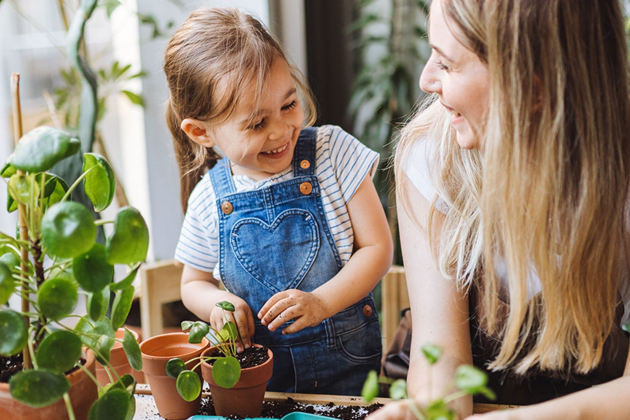 Junge Frau hält ihr lachendes Kind in den Armen, im Hintergrund eine Abflugtafel am Flughafen