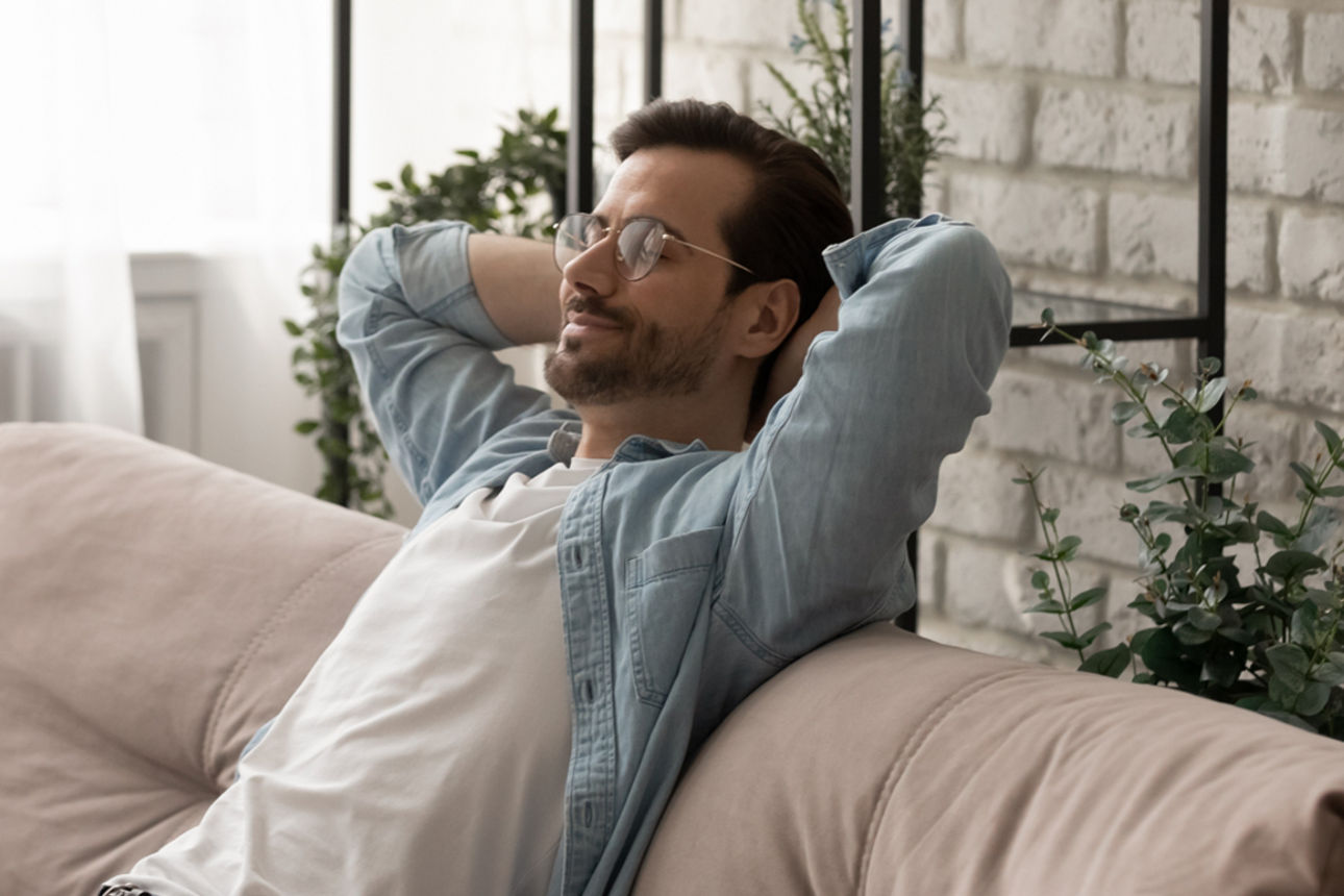 Mann sitzt entpannt auf der Coch mit den Händen über dem Kopf