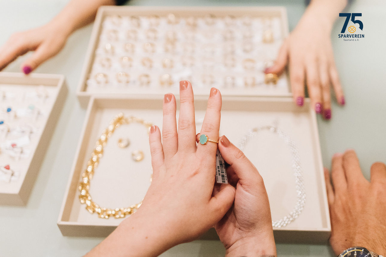 auf einem Tisch liegt eine Auswahl an Schmuck in zwei Kästchen und es sind mehrere Hände zu sehen