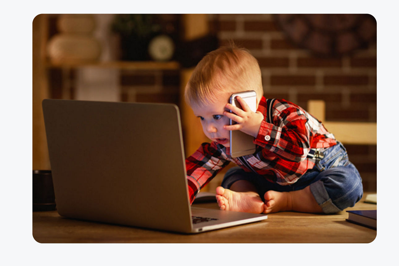 Ein Kind sitzt mit Handy am Ohr am Laptop