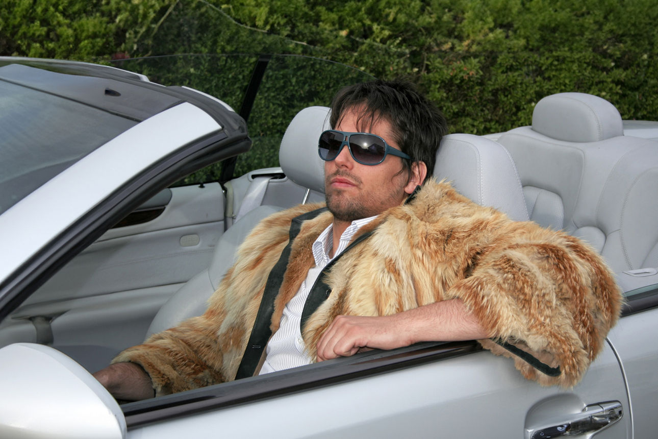 Ein Mann mit Sonnenbrille in Pelzjacke in einem Cabrio
