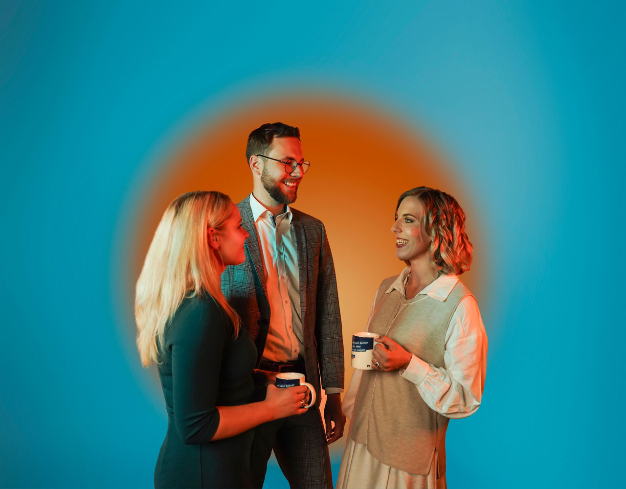 Zwei Frauen und ein Mann unterhalten sich vor einem blauen Hintergrund.