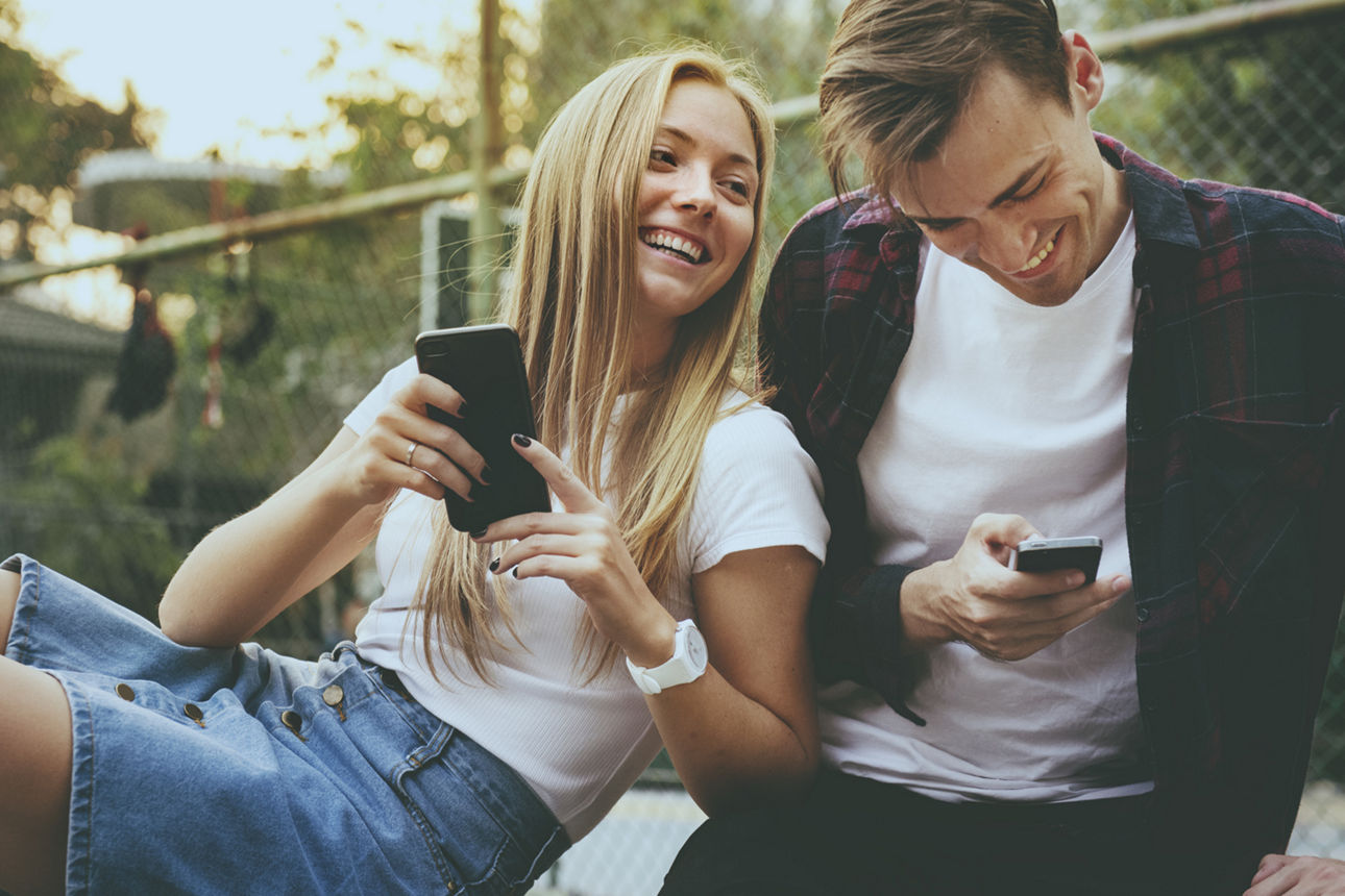 Junge Frau mit Smartphone in der Hand steht auf der Straße und lächelt