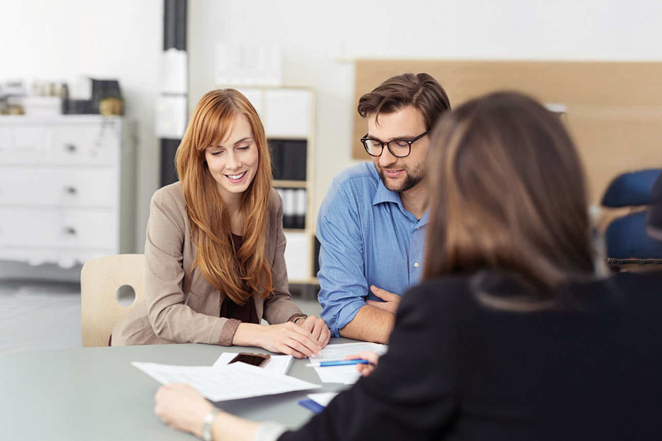 Junges Paaar sitzt an einem Tisch im Gespräch mit einer Kundenberaterin