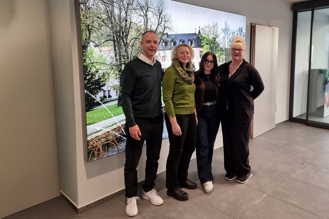 Vier Personen stehen nebeneinander in einem hellen Innenraum. Hinter ihnen hängt ein großformatiges Foto vom Schloss Wächtersbach. 