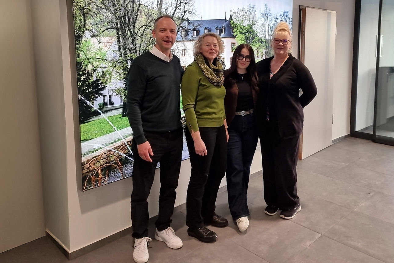 Vier Personen stehen nebeneinander in einem hellen Innenraum. Hinter ihnen hängt ein großformatiges Foto vom Schloss Wächtersbach. 