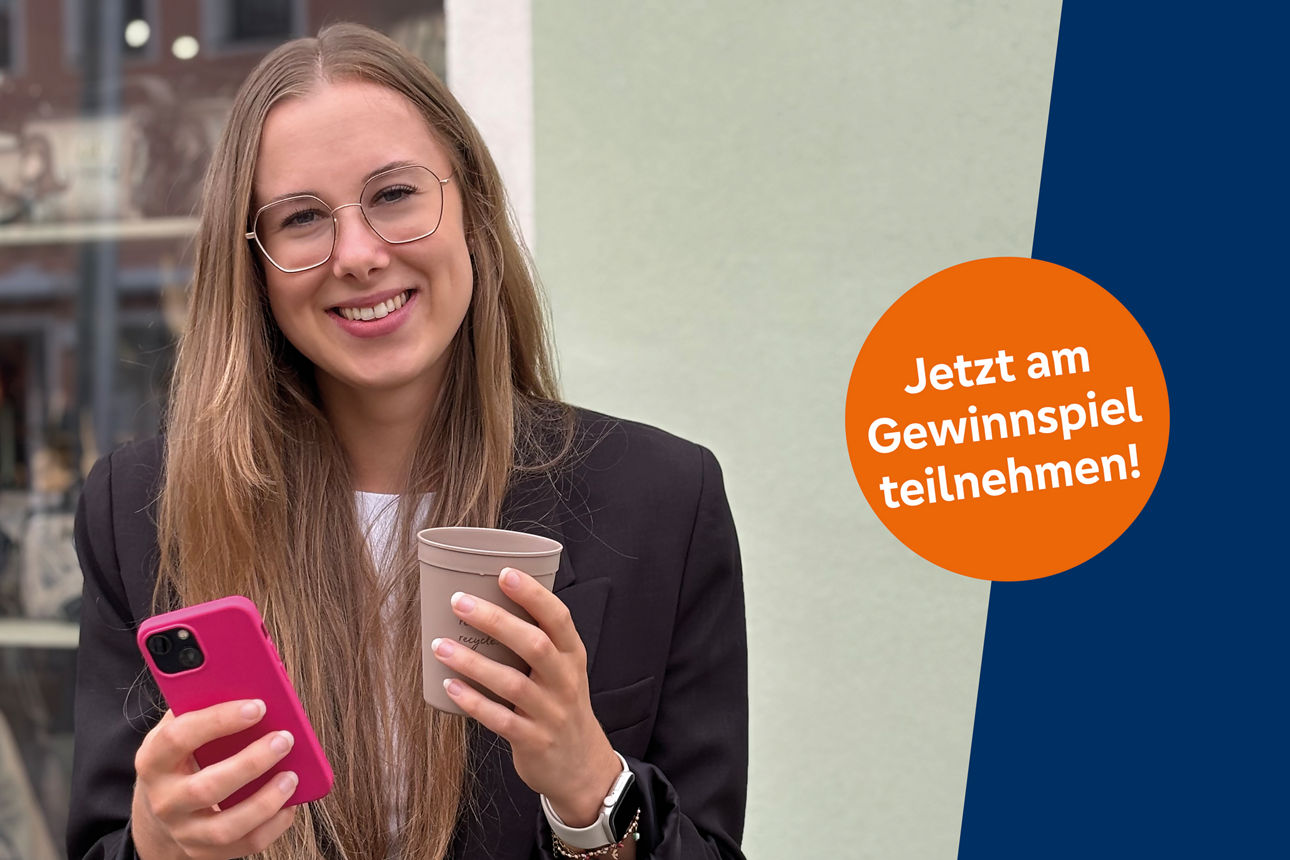 Junge Frau mit Cafe To-go-Becher und Smartphone in der Hand schaut in die Kamera
