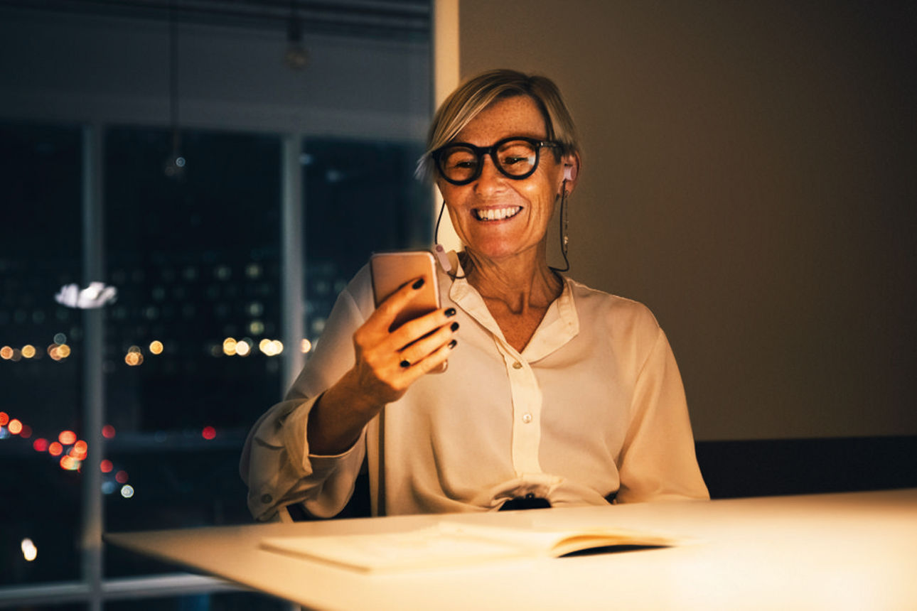 Eine Frau sitzt am Tisch und schaut in Ihr Smartphone