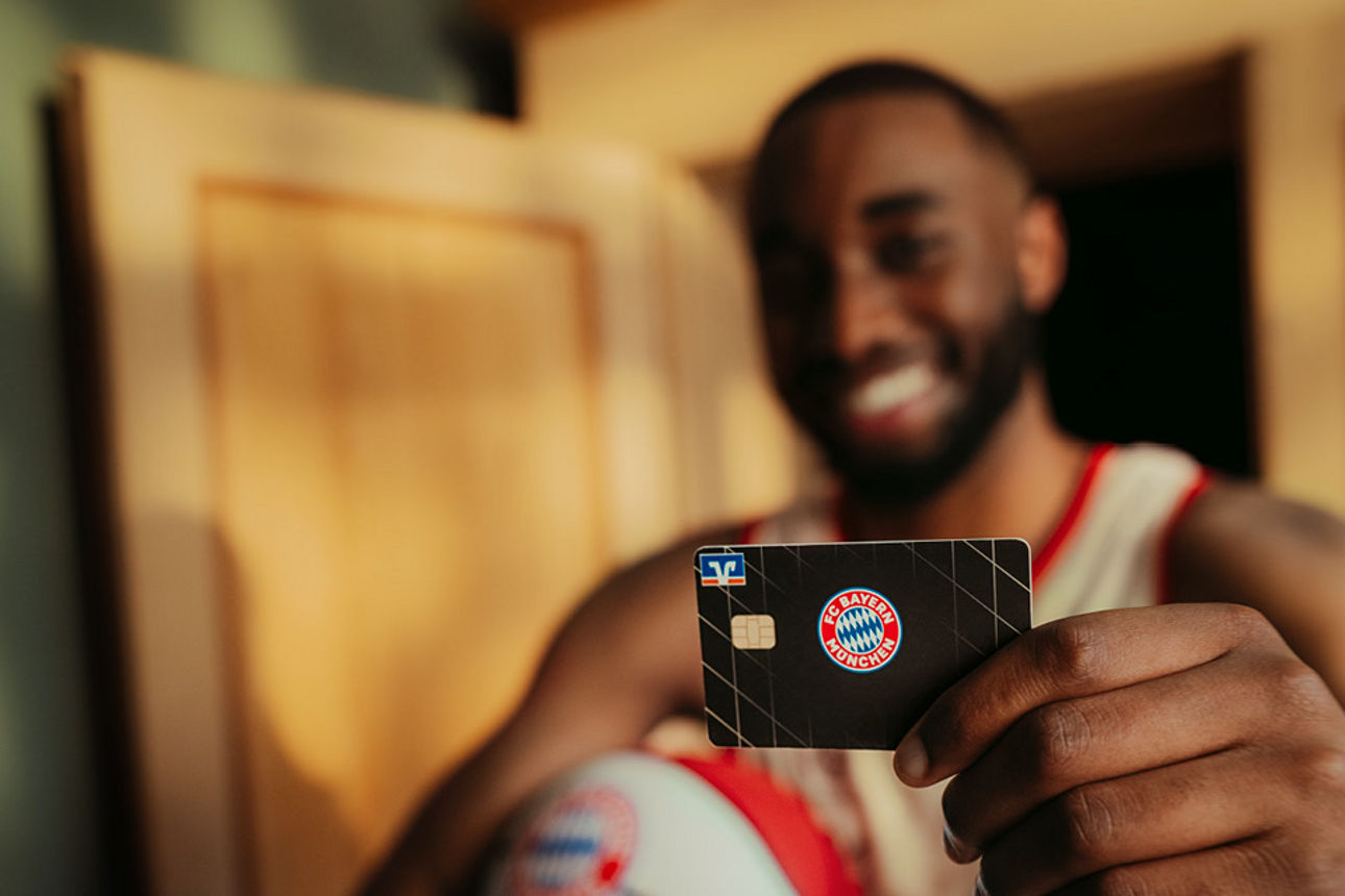 Ein Spieler des FC Bayern München Basketball hat die FC Bayern Kreditkarte in der Hand