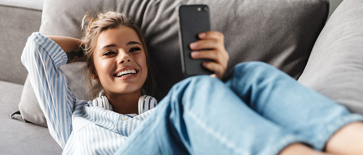 junge Frau liegt auf der Couch und schaut aufs Smartphone