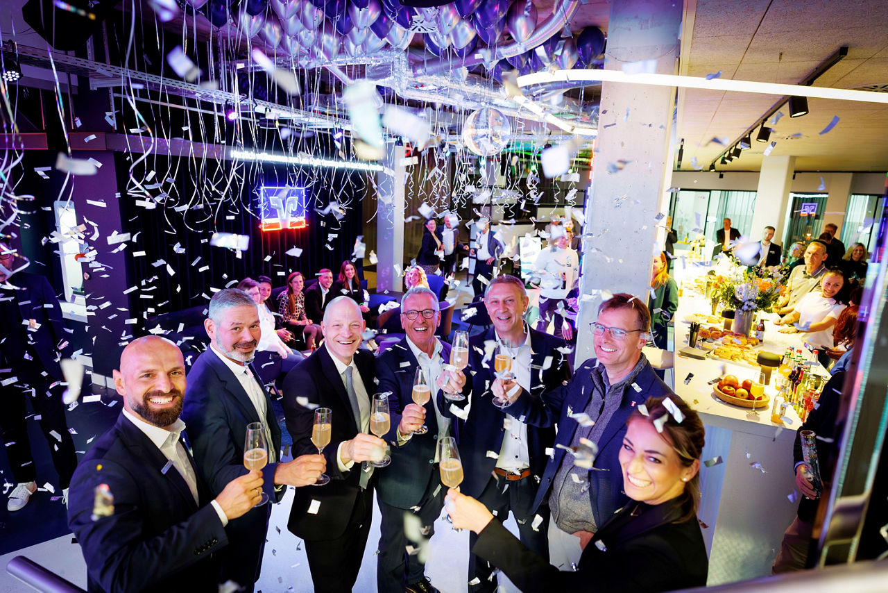 Gruppenfoto von Personen die feierlich ein Glas Sekt anstoßen im Konffeti Regen