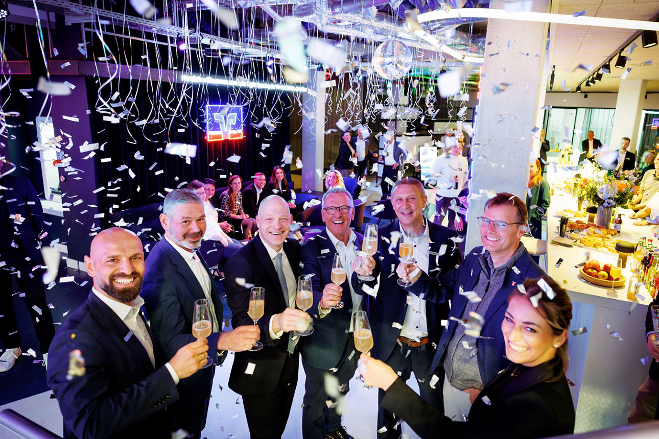 Gruppenfoto von Personen die feierlich ein Glas Sekt anstoßen im Konffeti Regen
