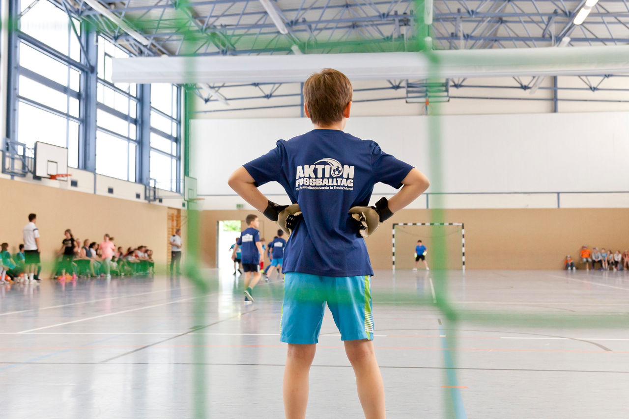 Weibliches Kind steht mit ausgebreiteten Armen vor einem Fußballtor