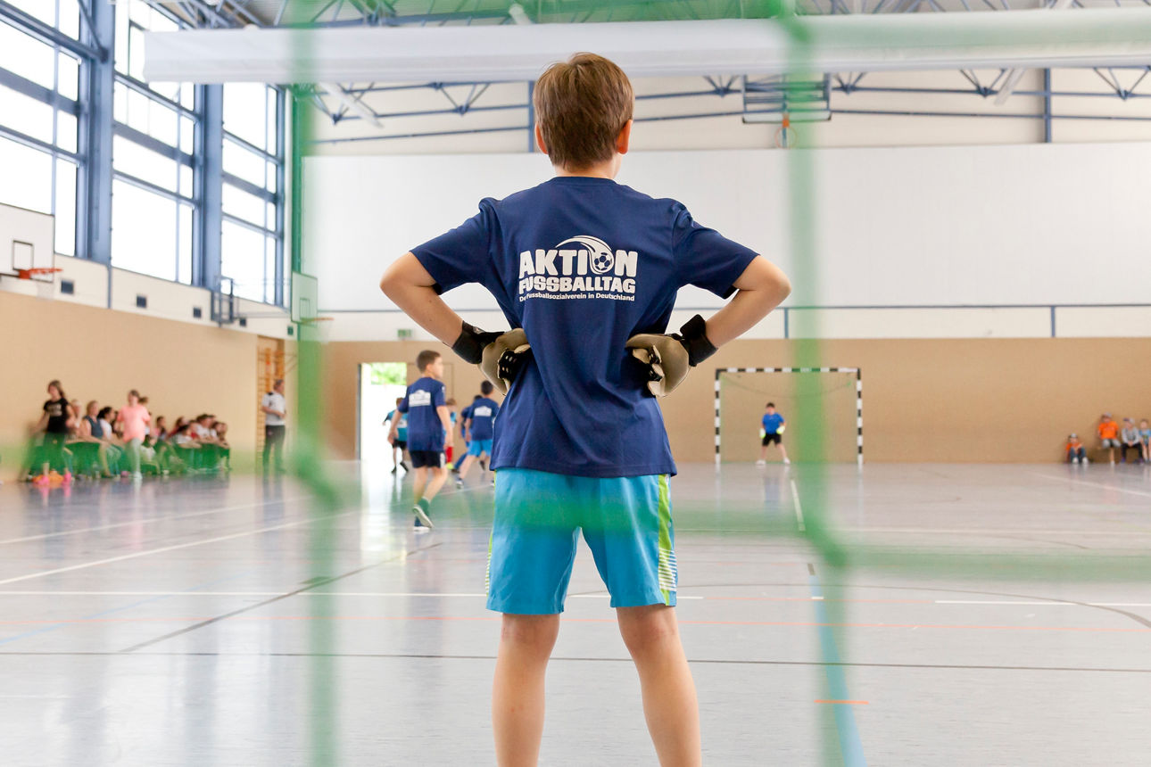 Weibliches Kind steht mit ausgebreiteten Armen vor einem Fußballtor