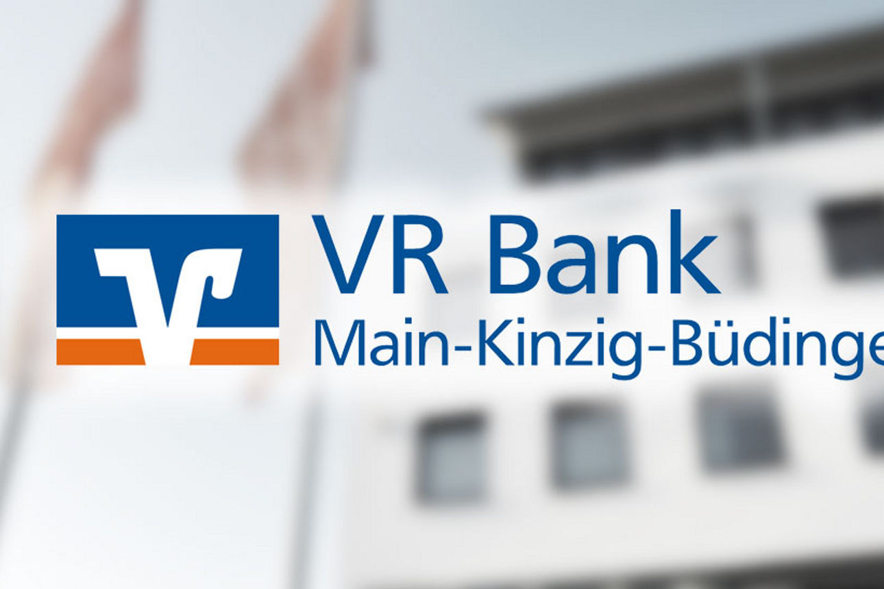 Im Hintergrund unscharf das Gebäude der ehemaligen VR Bank Main-Kinzig-Büdingen in Altenhaßlau, im Vordergrund das Logo