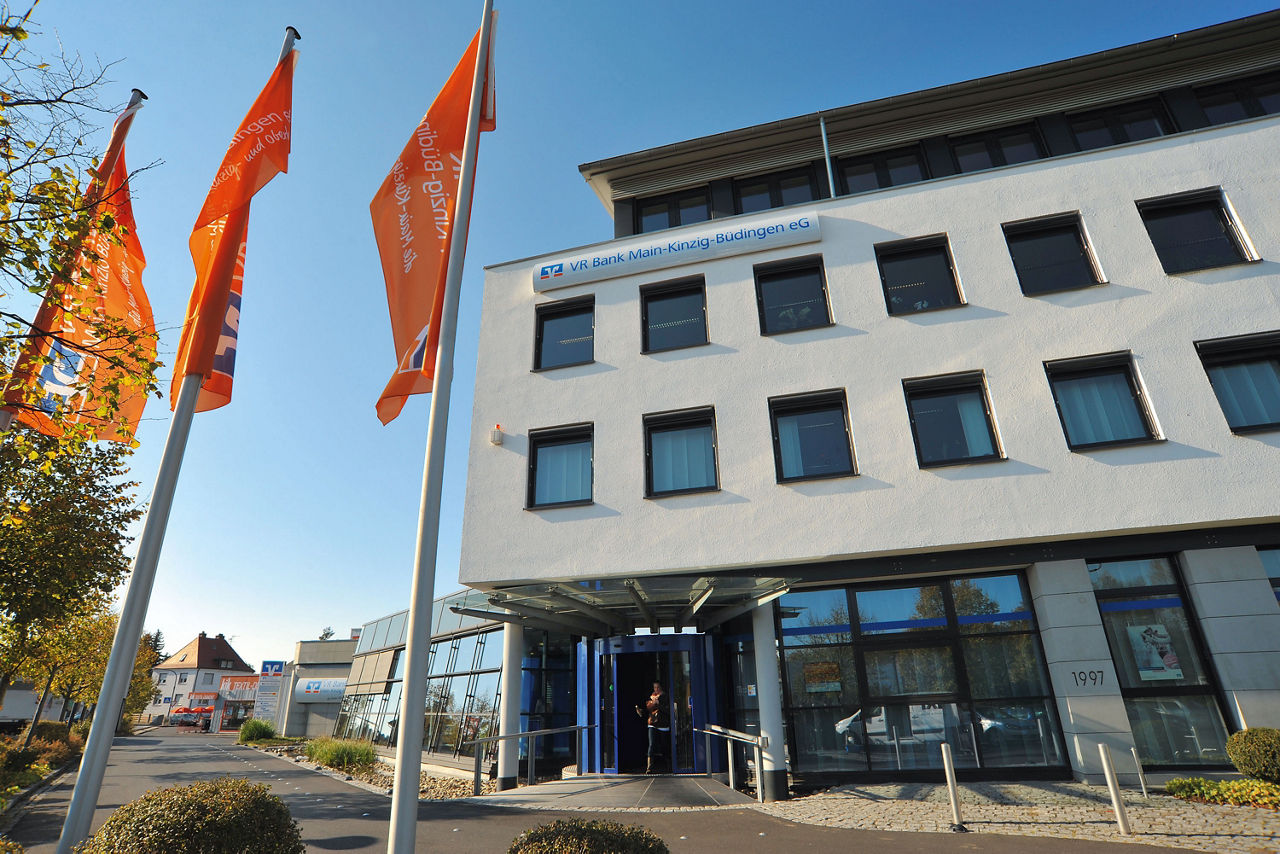 Außenansicht des Bankgebäudes in Linsengericht-Altenhaßlau mit Fahnen im Vordergrund.