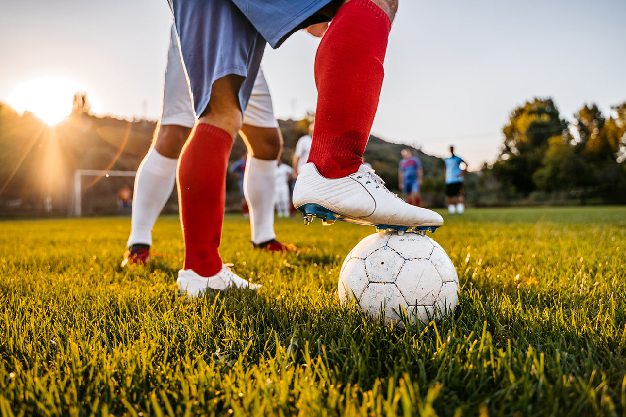 Bild von den Beinen von Fußballer mit weißem Fußball auf grüner Wiese