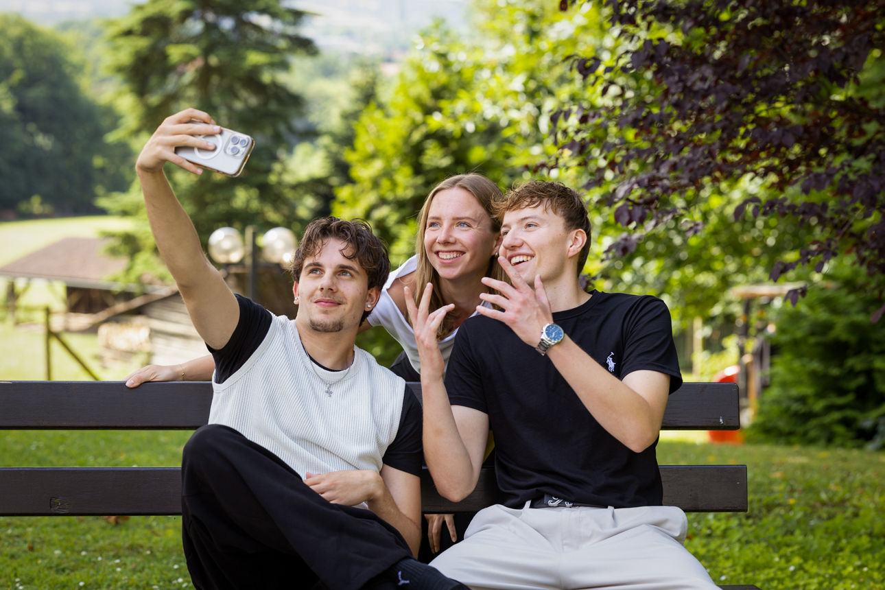 3 junge Menschen sitzen auf einer Bank und machen ein Selfie