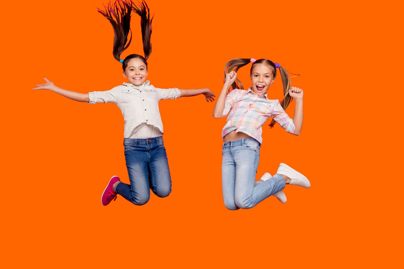 zwei springende Mädchen vor einem orangefarbenen Hintergrund
