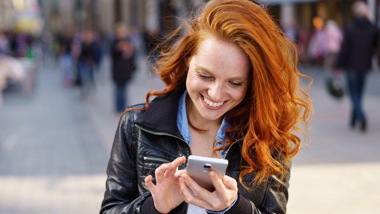 Frau mit roten Haaren schaut auf ihr Handy