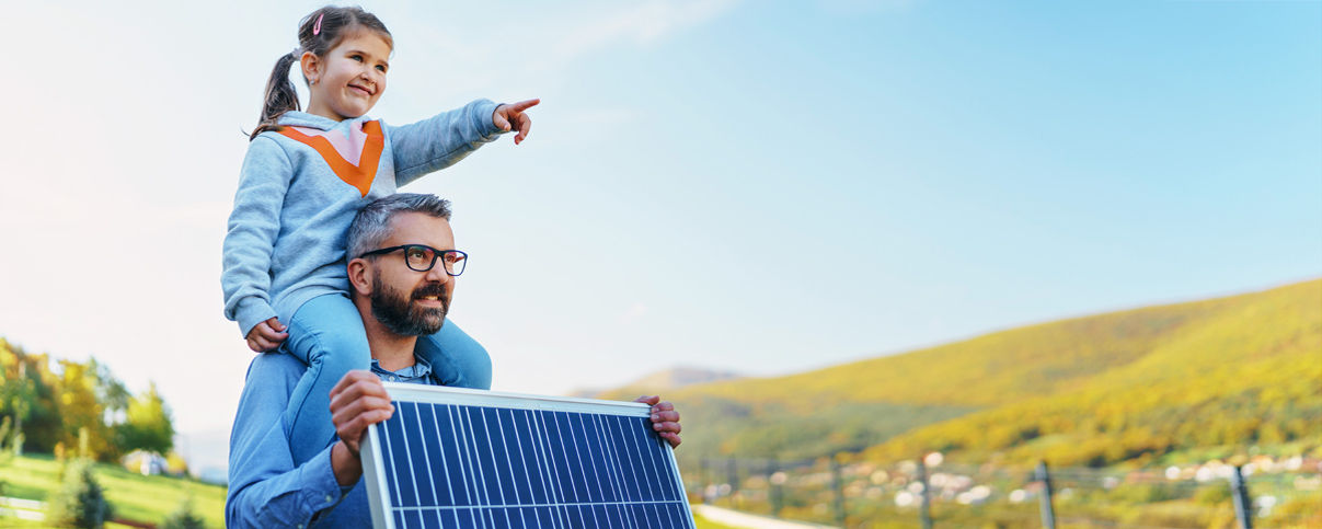Tochter sitzt auf Schultern von Vater mt Solarplatte in den Händen