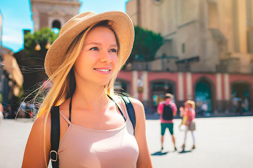 Junge Frau mit Sonnenhut auf dem Kopf und Rucksack steht auf einem Marktplatz