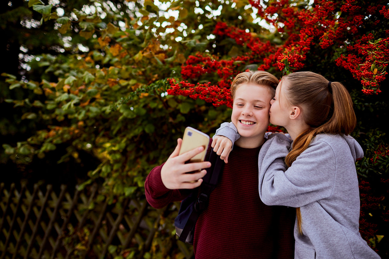 Junge und Mädchen machen ein Selfie, wobei das Mädchen dem Jungen einen Kuss auf die Wange gibt - Symbolbild für Jugendsparko