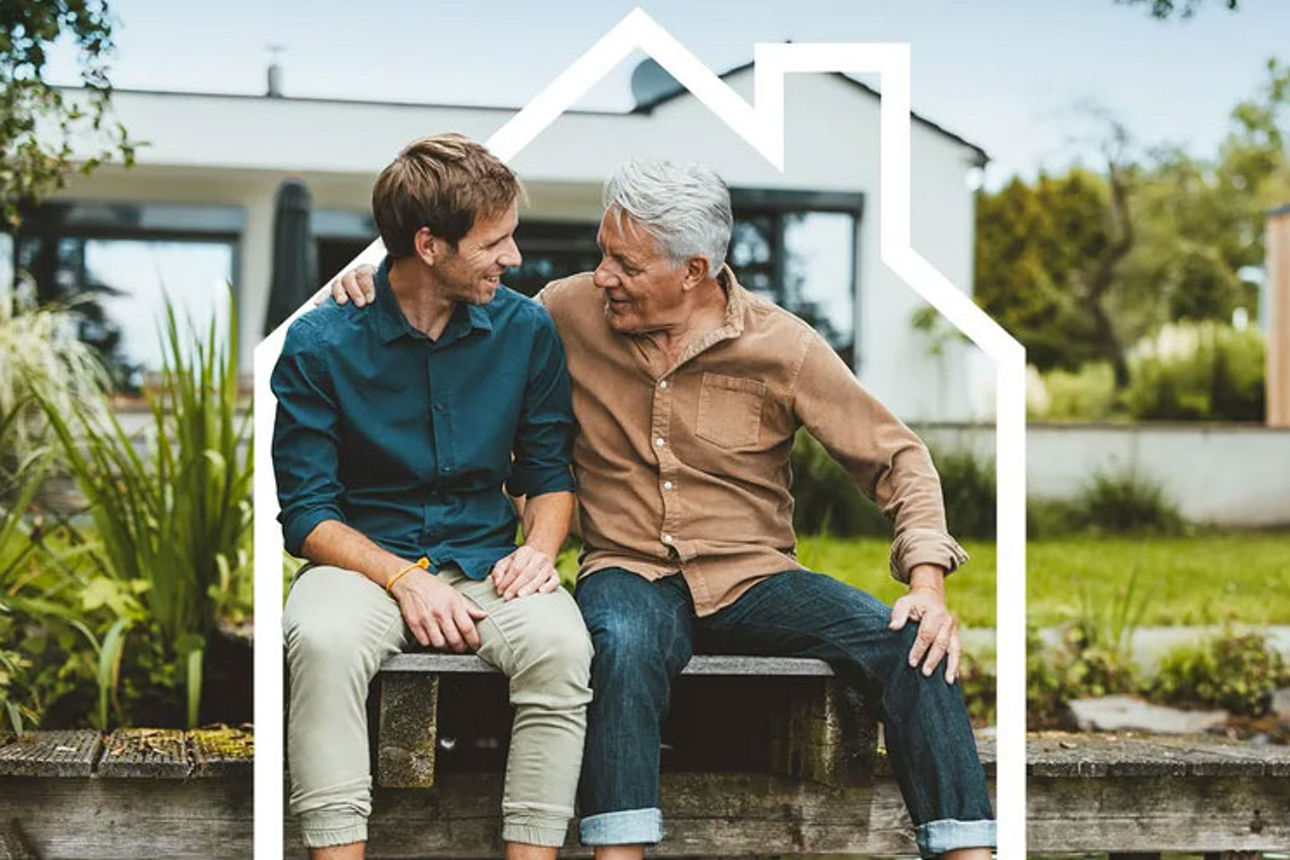 Erwachsener Sohn und Vater sitzen auf Steg vor einem Haus