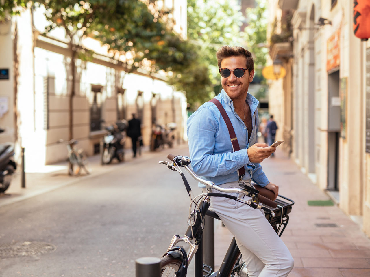 Ein Mann mit Sonnenbrille lehnt an seinem Fahrrad und hält ein Handy in der Hand.