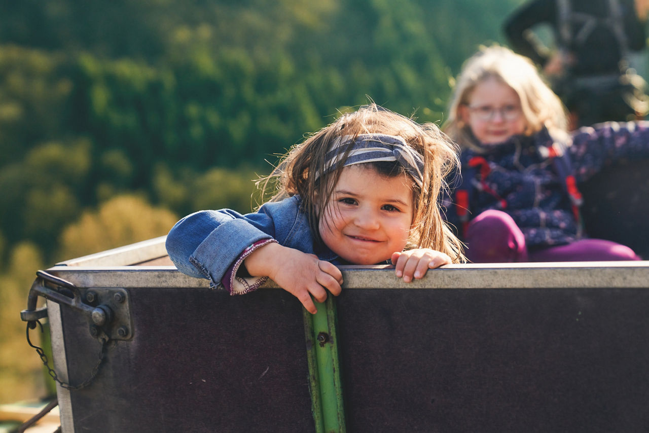Zwei Kinder sitzen in einem Traktor-Anhänger in den Weinbergen