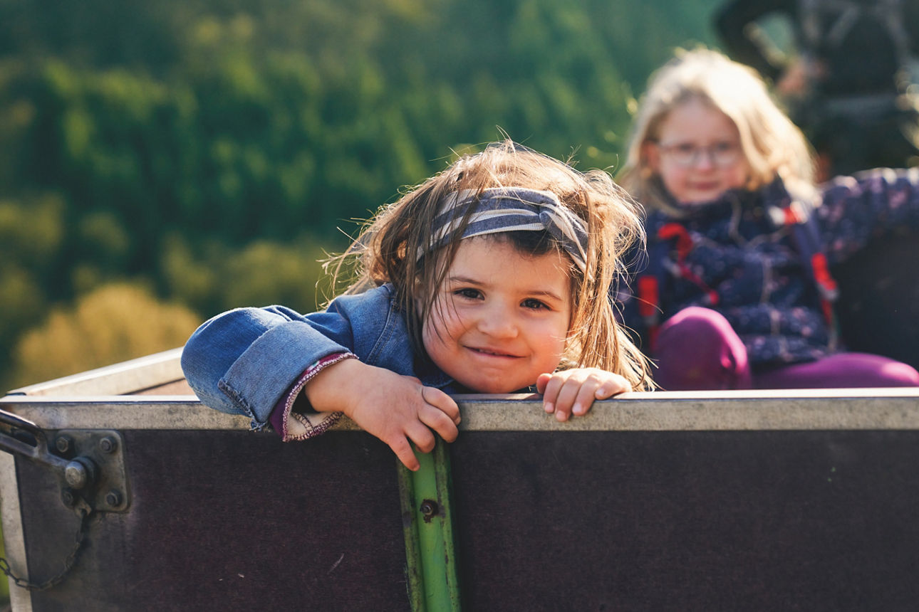 Zwei Kinder sitzen in einem Traktor-Anhänger in den Weinbergen