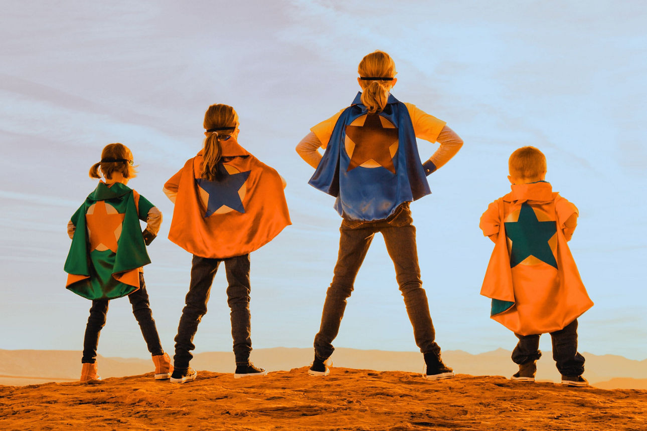 Kinder stehen als Superhelden mit Capes in einer Landschaft und symbolisieren Mut, Zusammenhalt und eine starke Zukunft