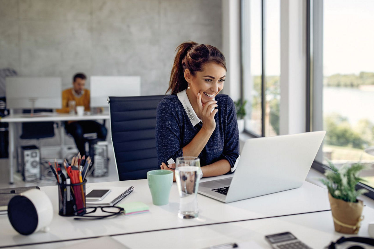 Eine junge Dame sitzt vor einem Laptop und lächelt